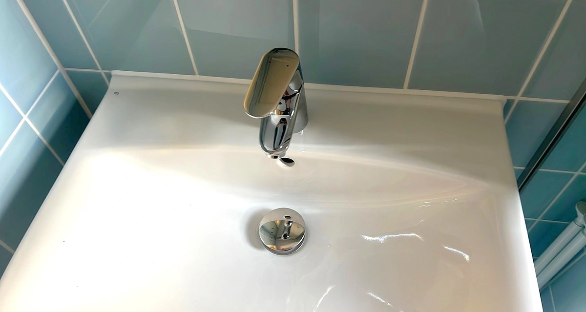 Hvid sanitetsfuge mellem håndvask og blå flisevæg på Fynshuse i København NV